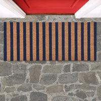 Striped doormat with blue and brown stripes on a stone floor in front of a red door.