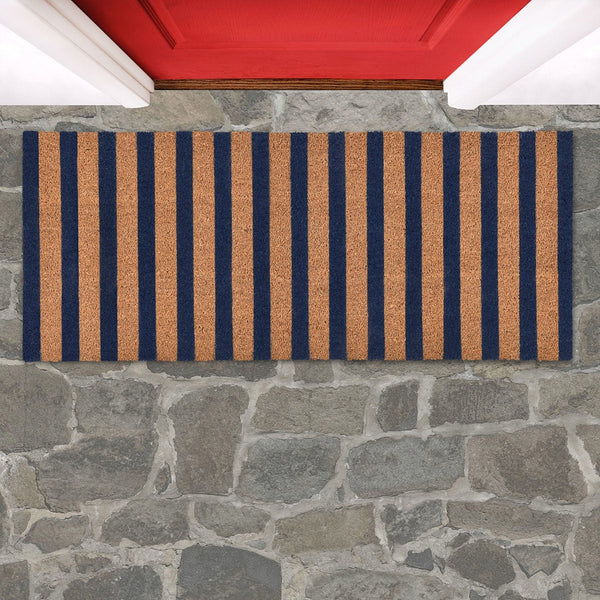 Striped doormat with blue and brown stripes on a stone floor in front of a red door.