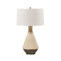 A table lamp with a tapered ceramic base in cream and dark brown, topped with a white drum shade and a small metallic finial.