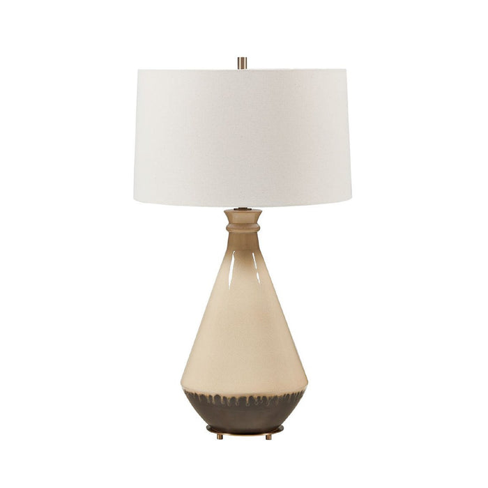 A table lamp with a tapered ceramic base in cream and dark brown, topped with a white drum shade and a small metallic finial.