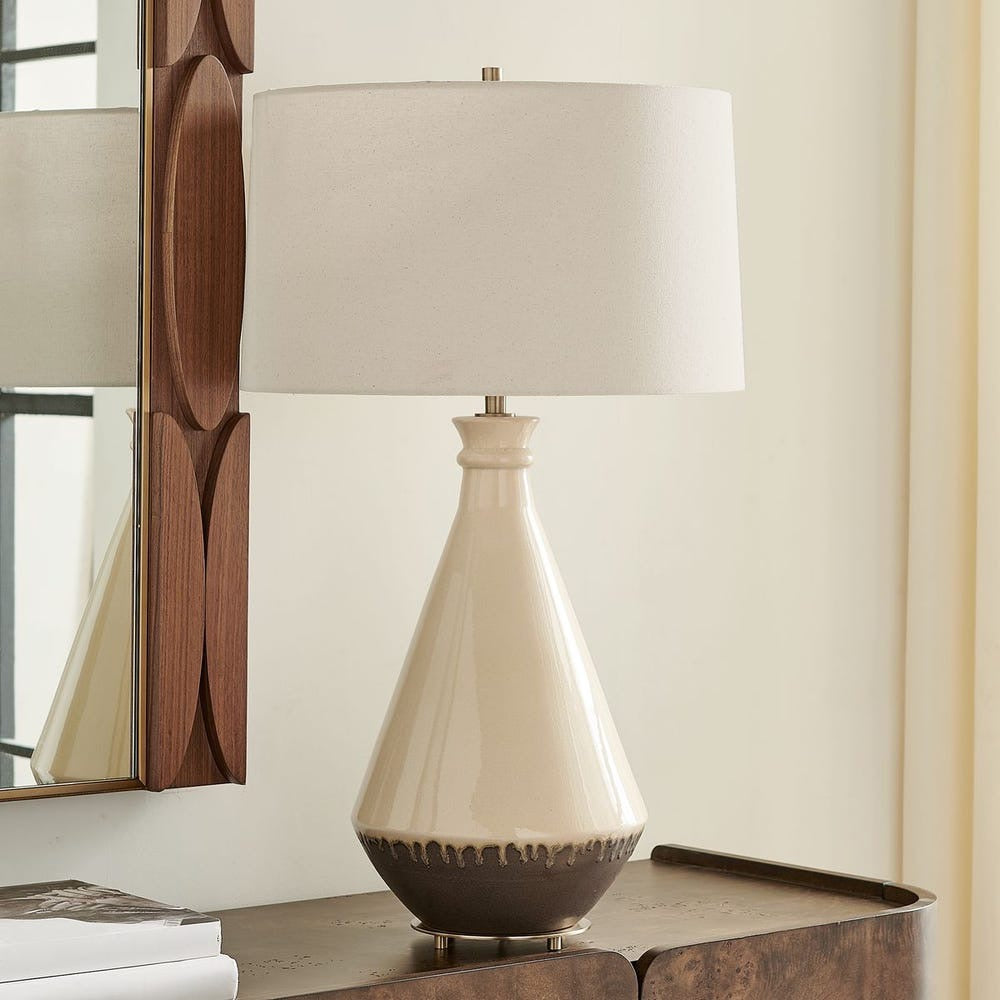 Beige ceramic table lamp with a white shade on a wooden surface.