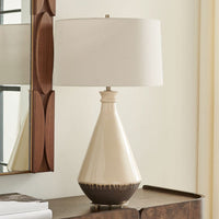 Beige ceramic table lamp with a white shade on a wooden surface.