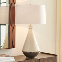 Decorative lamp with a white shade on a wooden surface next to a mirror.