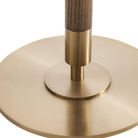 Close-up of a table lamp base with a round brushed brass plate, a matching central collar, a dark wood-grain vertical stem, and a small brass finial on a white background.