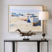 Beached Boats Framed Print by Uttermost hangs above a black console table with a lamp and driftwood sculpture.