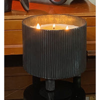 A lit Blacksmith Forged Candle by Himalayan Trading Post on a reflective surface, soy wax blend in ribbed black vessel.