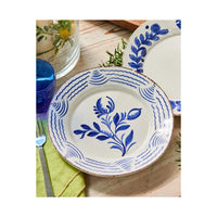 White plate with blue floral design on a wooden table with a glass and fork.