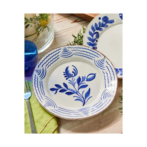 White plate with blue floral design on a wooden table with a glass and fork.