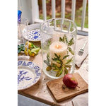 Decorative candle in a glass holder on a table with plates and fruit