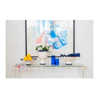 Decorative table setting with a vase, fruits, and candles in front of abstract art.
