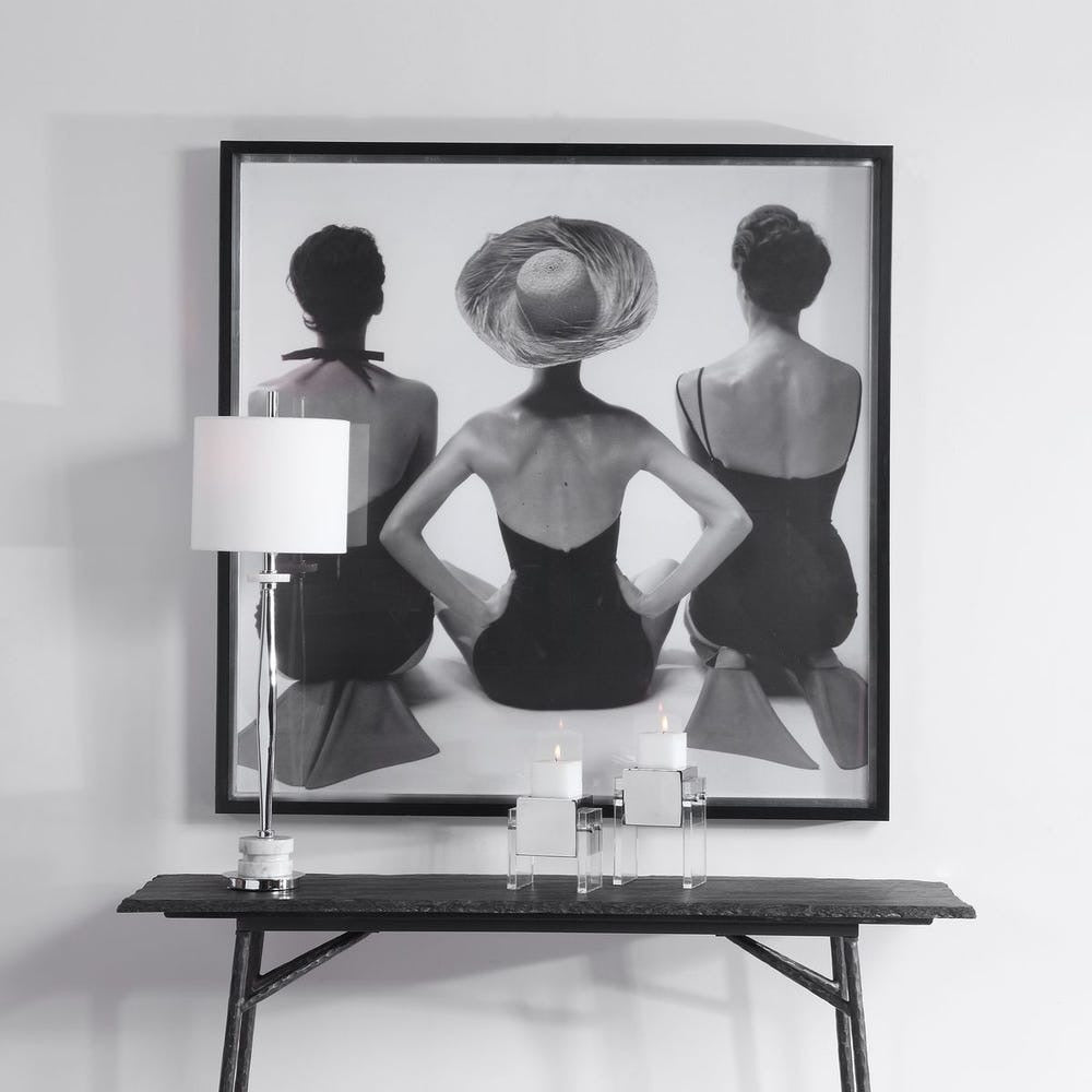 Framed black and white art print of three women on a wall above a console table.