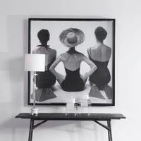 Framed black and white art print of three women on a wall above a console table.