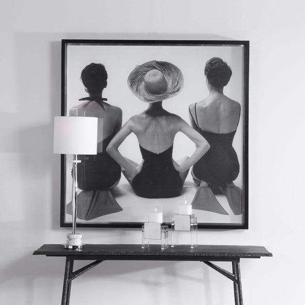 Framed black and white art print of three women on a wall above a console table.