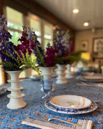 Elegant table setting with floral arrangements, Abigails Blue Skies Cabana tablecloth, and blue and white plates in a cozy room.