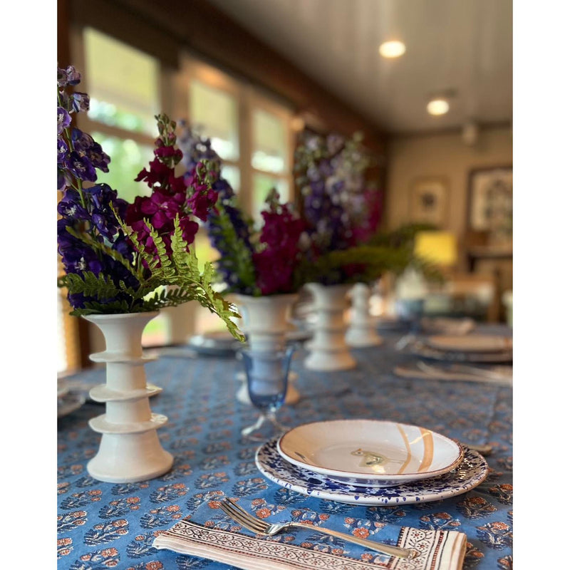 Elegant table setting with floral arrangements, Abigails Blue Skies Cabana tablecloth, and blue and white plates in a cozy room.