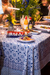 A table with sushi, flowers, and condiments on an Abigails Beach Chic Cabana Tablecloth, surrounded by guests serving themselves.