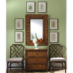 bamboo wall mirror above rattan chest and two bamboo chairs on green painted wall