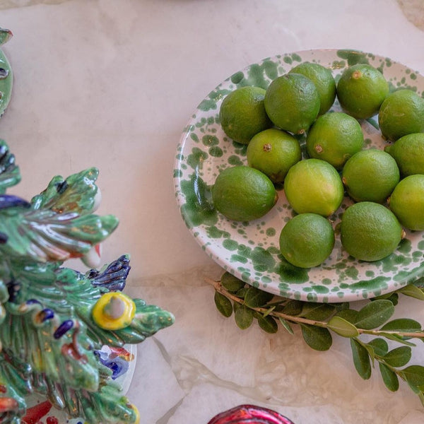Green limes on a decorative plate with a ceramic bird figurine and green leaves.