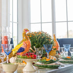 Decorative Thanksgiving table setting with colorful turkey figurines, glasses, and a floral arrangement.