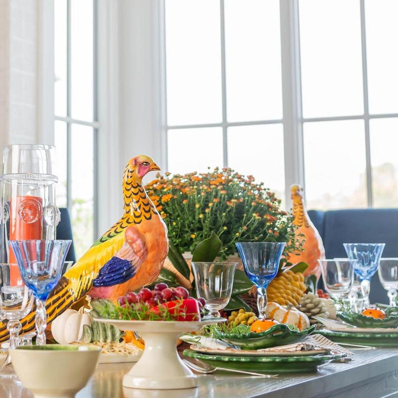 Decorative Thanksgiving table setting with colorful turkey figurines, glasses, and a floral arrangement.