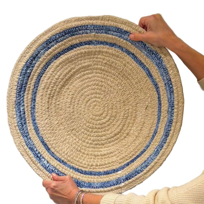 Round woven mat with blue border held by a person on a white background