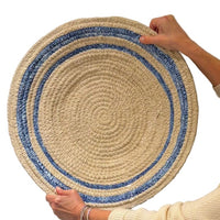 Round woven mat with blue border held by a person on a white background