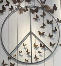 Sugarboo & Co. Hanging Metal + Jute Peace Sign displayed on a white wall with decorative butterflies.