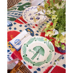 Colorful table setting with decorative plates and flowers on a patterned tablecloth.