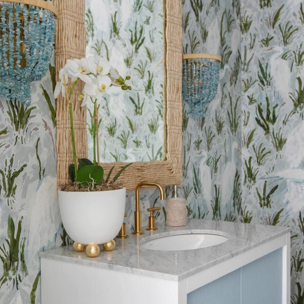 Bathroom vanity with marble top, gold accents, Abigails Catalina Matte Off White Footed Cachepot, and botanical wallpaper.
