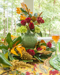 Decorative floral arrangement with a green vase on a table outdoors.