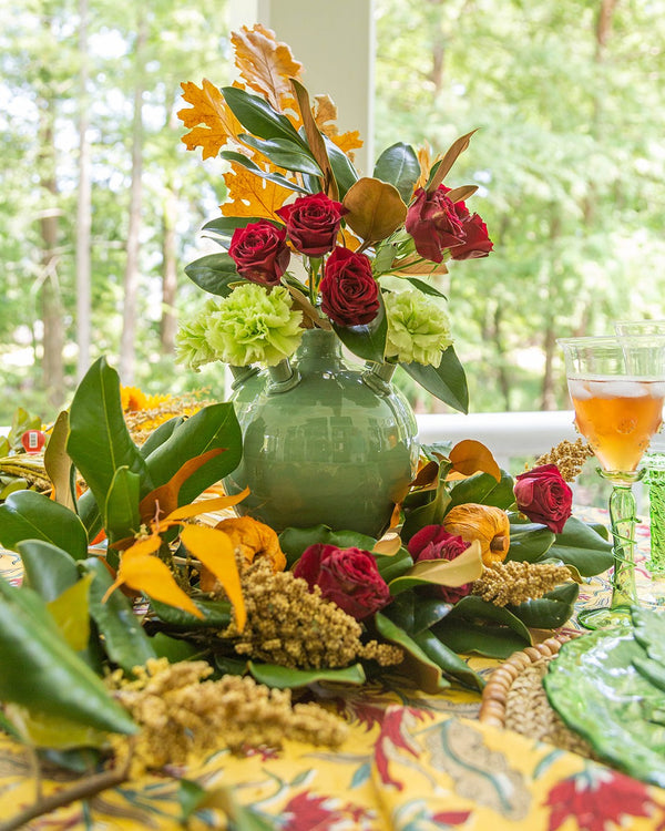 Decorative floral arrangement with a green vase on a table outdoors.
