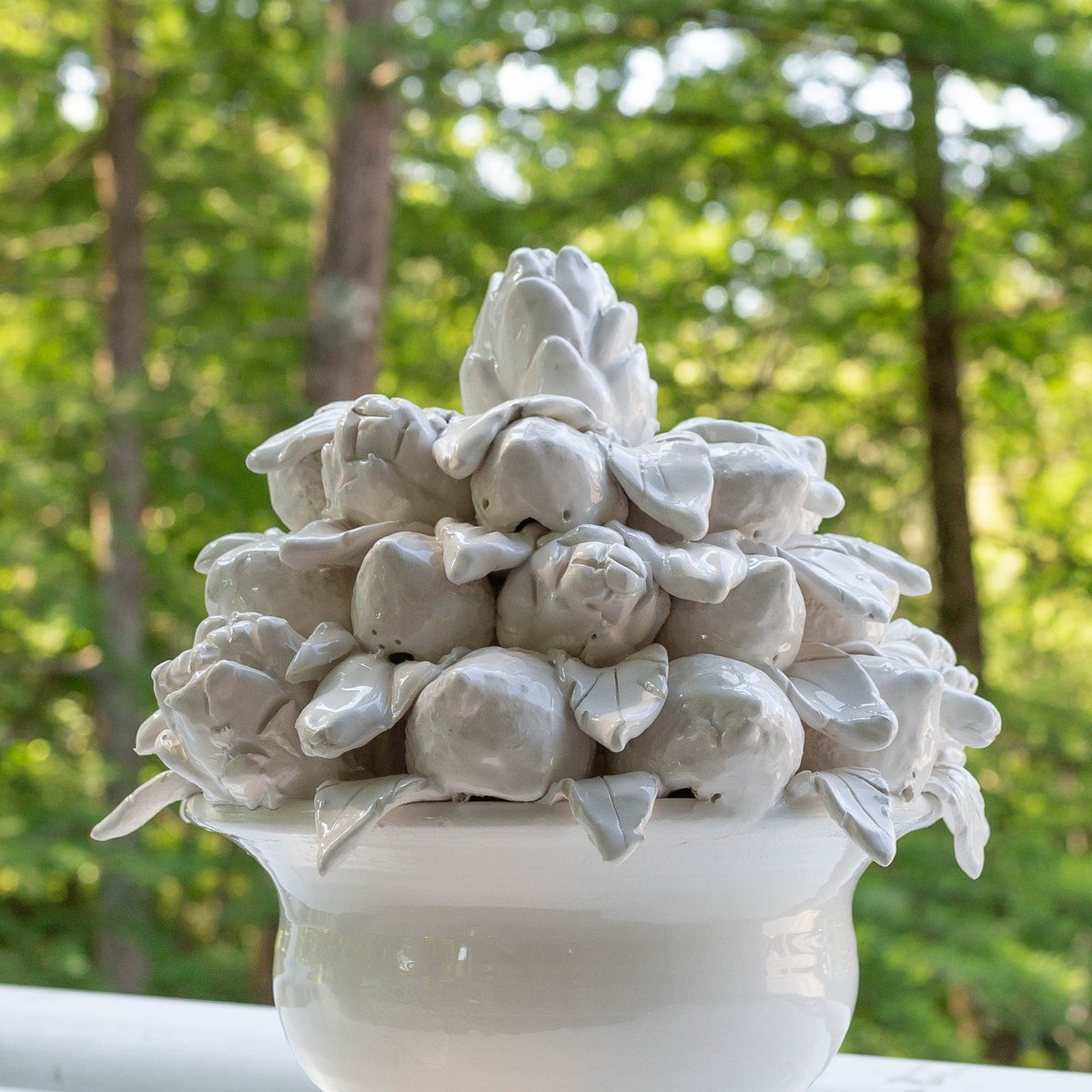 Decorative stone sculpture resembling a flower in a white vase against a green forest background