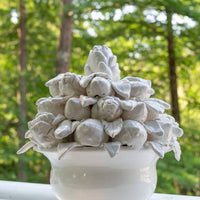 Decorative stone sculpture resembling a flower in a white vase against a green forest background