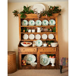 Wooden dresser with decorative plates, fruits, and a deer head in a room.