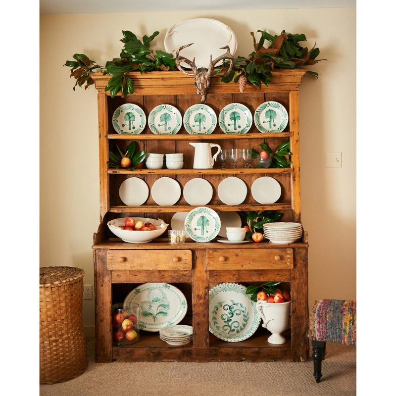 Wooden dresser with decorative plates, fruits, and a deer head in a room.