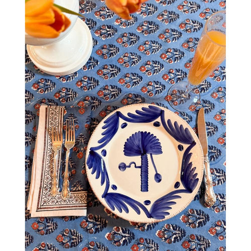 Decorative table setting with blue and white plate, cutlery, and orange flowers on a patterned tablecloth.
