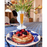 Pancakes with berries are served on Abigails Casa Nuno Blue Palm Dinner Plates beside a mimosa and tulips.