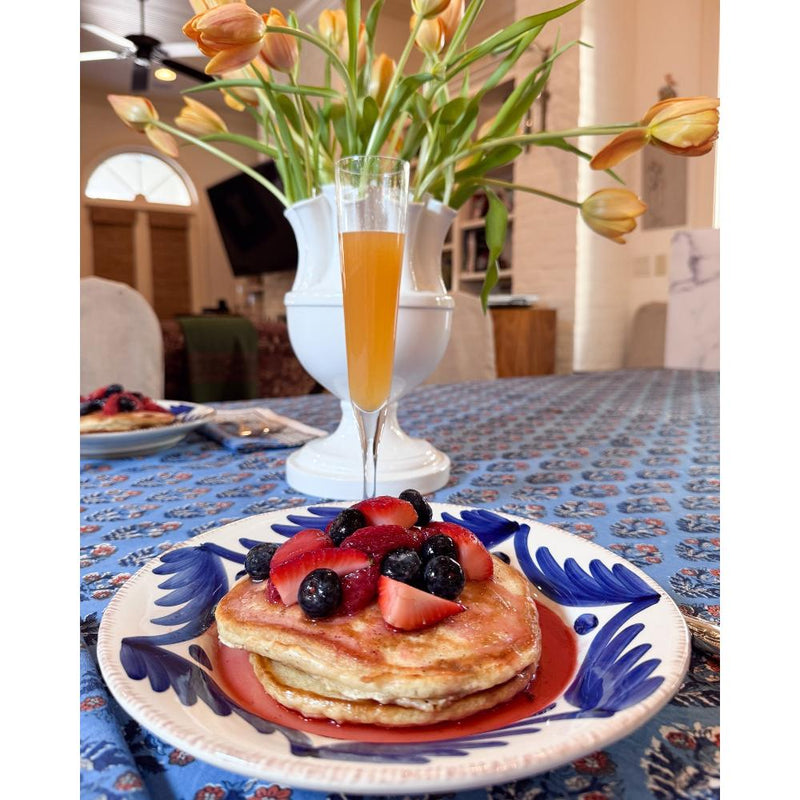 Pancakes with berries are served on Abigails Casa Nuno Blue Palm Dinner Plates beside a mimosa and tulips.