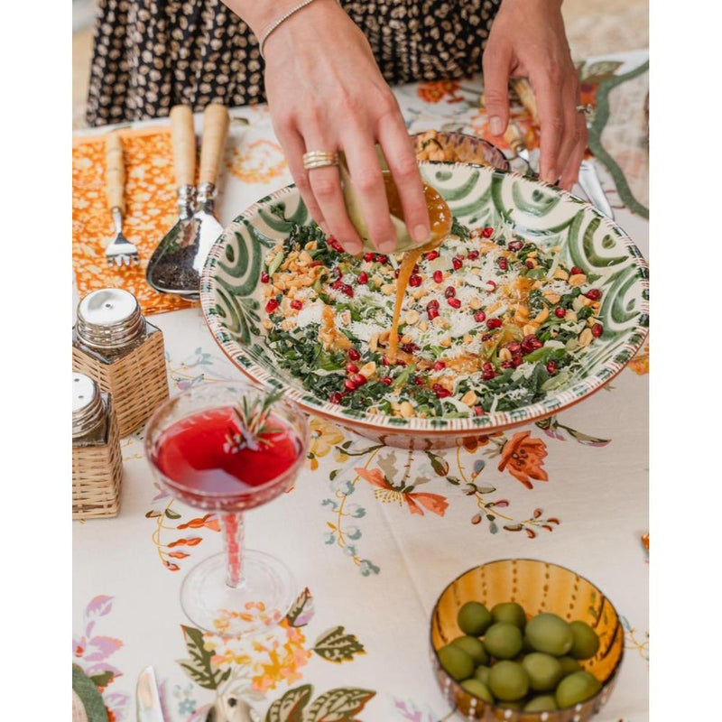 Person garnishing a dish with a colorful tablecloth and glasses in the background