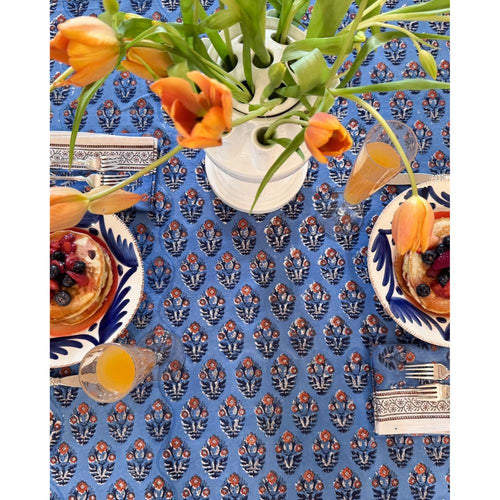 Decorative table setting with a blue patterned tablecloth, plates with food, and a vase with flowers.
