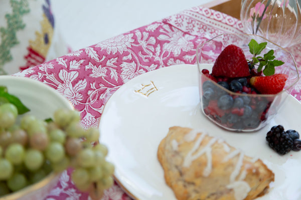 Dessert plate with pastries, berries, and a glass of water on a patterned tablecloth.