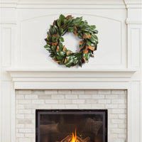 A Grand Magnolia Leaf Wreath from Napa Home & Garden hangs above a white brick fireplace with a burning fire in the hearth, perfect for interior use.