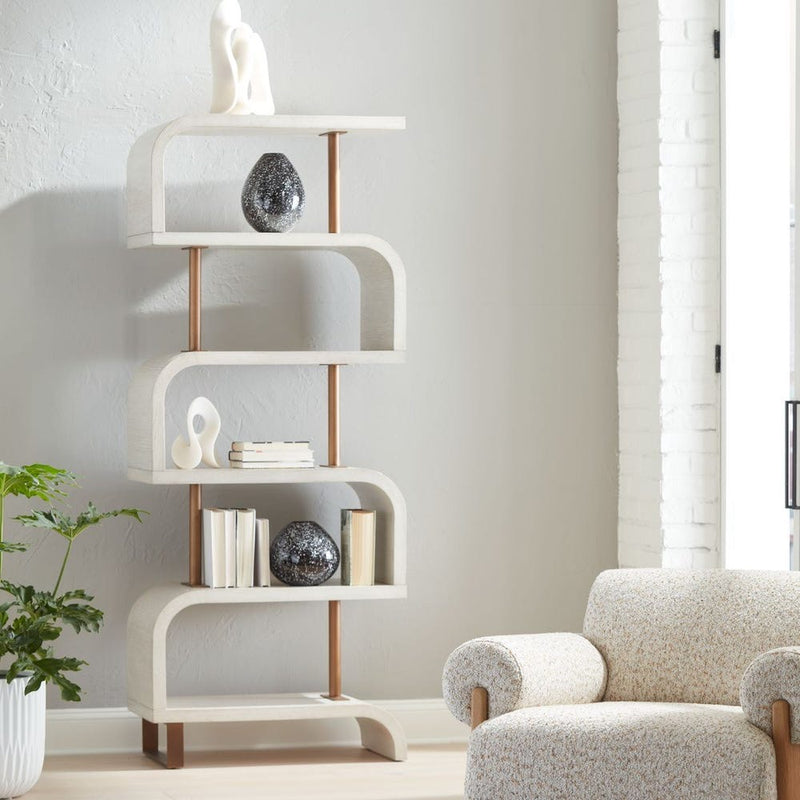 The Uttermost Bia White Etagere with abstract decor, books, and a speckled armchair stands by a large window.