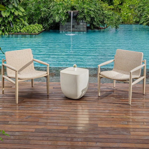 Two wicker chairs and a small table on a wooden deck by a pool with a fountain.