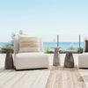 Modern outdoor seating area with white chairs and a Classic Home Collins Concrete Accent Table, ocean view in background.
