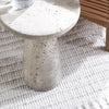 The Collins Concrete Accent Table by Classic Home in rust on a white rug beside wooden furniture.