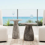 Two Classic Home Collins Concrete Accent Tables, set with wine glasses between white chairs by the ocean.
