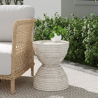 Woven patio furniture and the Classic Home Corey Outdoor Accent Table with a plant, on a patio with green shrubs.