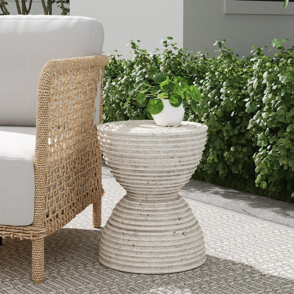 Woven patio furniture and the Classic Home Corey Outdoor Accent Table with a plant, on a patio with green shrubs.