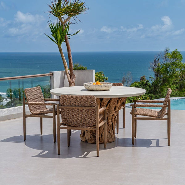 Outdoor dining set with a round table and chairs on a patio overlooking the ocean.
